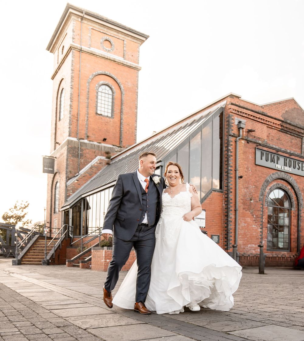 Wedding couple posing outside a vintage brick pump house building with arched windows.
