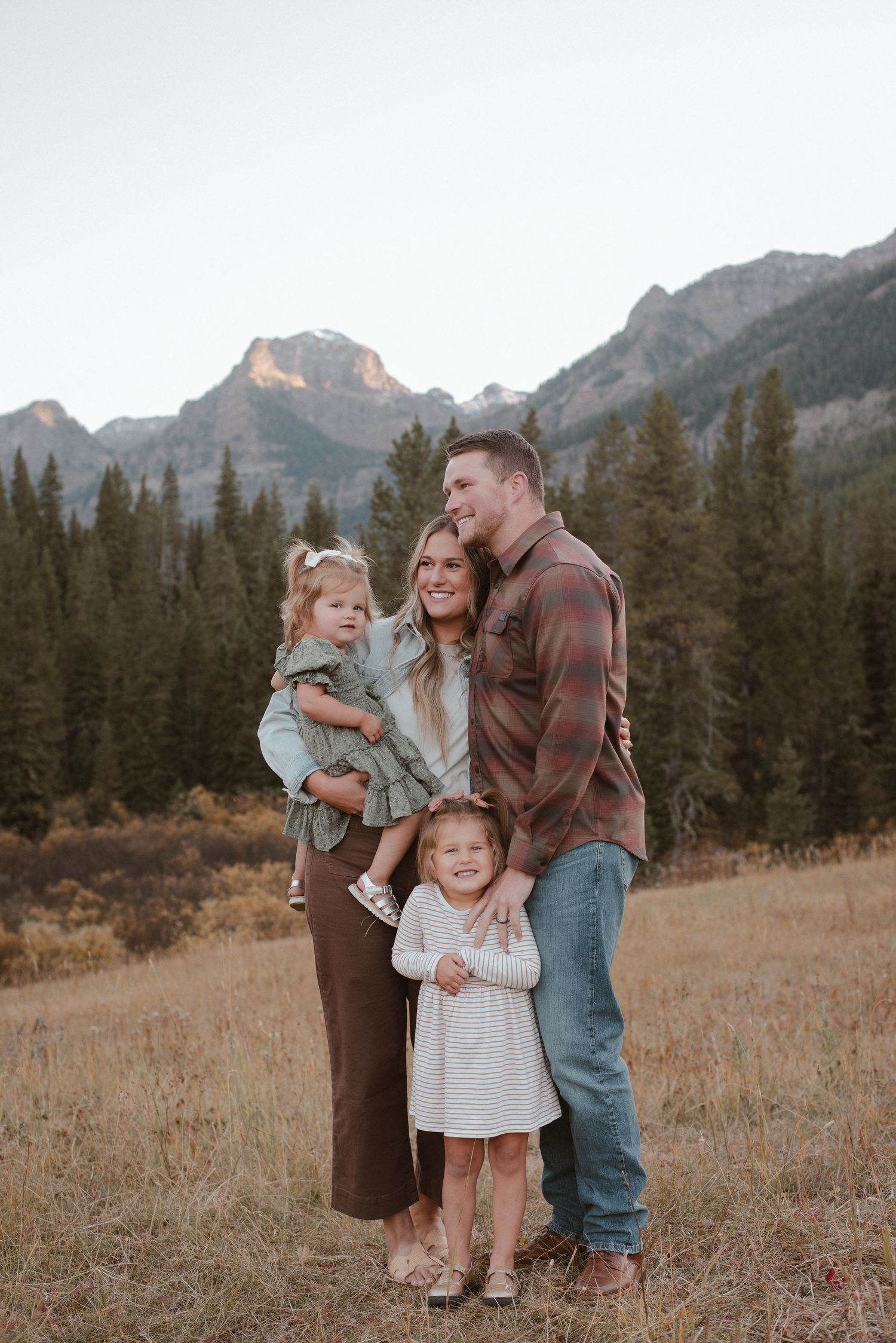 A sweet family portrait captured against a backdrop of majestic mountain peaks and evergreen forest.