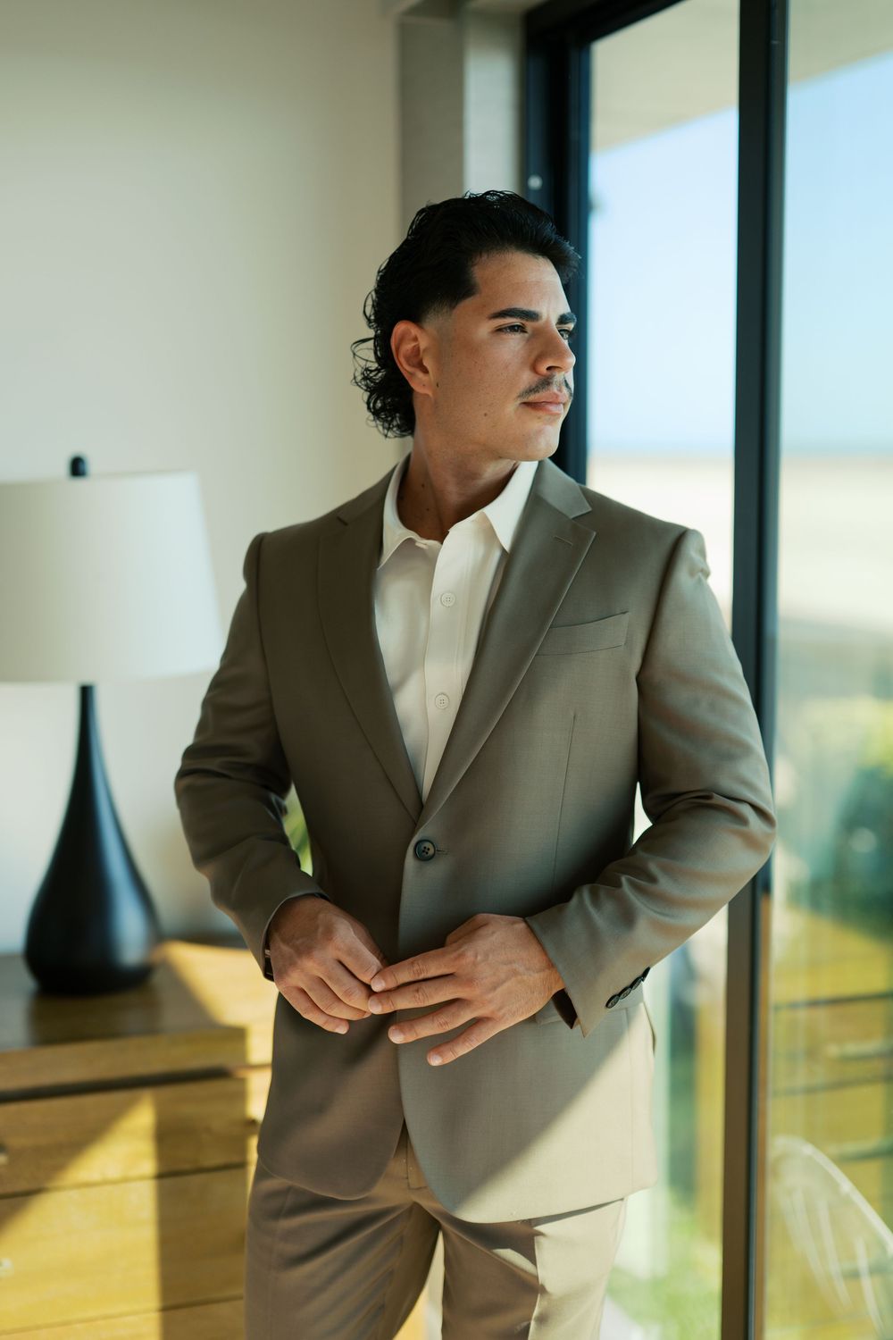 A person wearing a gray suit and white shirt poses near windows in multiple shots showing different angles.