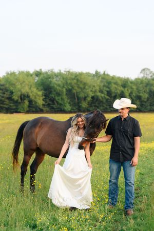 A couple stands in a green field with their horse during a romantic countryside engagement photo session.