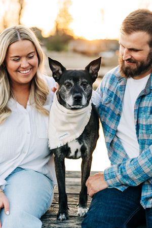 A couple spends time outdoors with their black and white Boston Terrier dog during sunset.