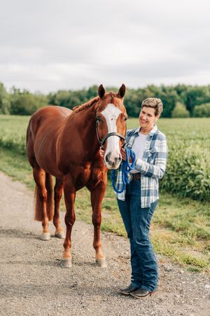 Person in blue overalls bonding with a beautiful chestnut horse with white markings on a country path.