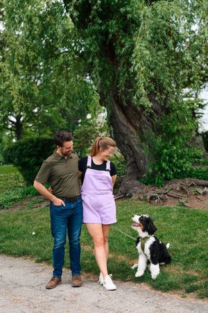 A couple petting their black and white border collie dog while walking on a grassy path near trees.