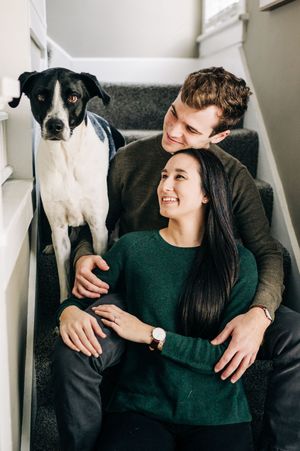 A love-filled photoshoot shows affectionate moments between a couple and their sweet black and white dog on a couch.