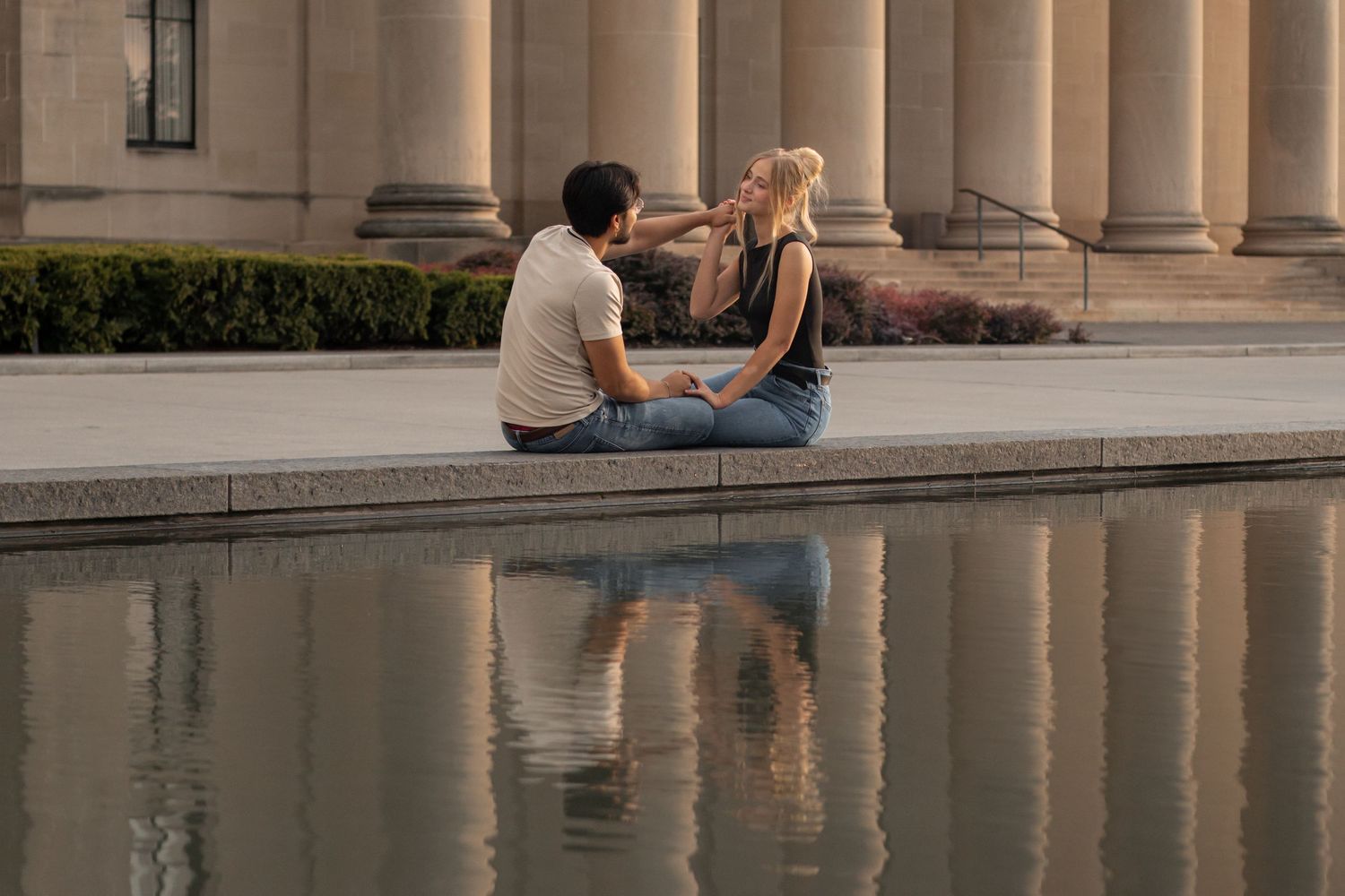 Couple sitting by a reflective pool at sunset creating romantic silhouettes against classical architecture.