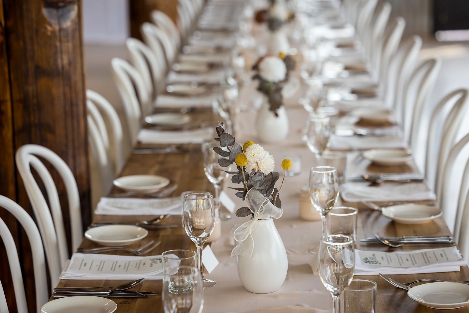 Elegant table setting with white bentwood chairs and floral centrepieces in white vases along a rustic linen tablecloth at Buller Wines.