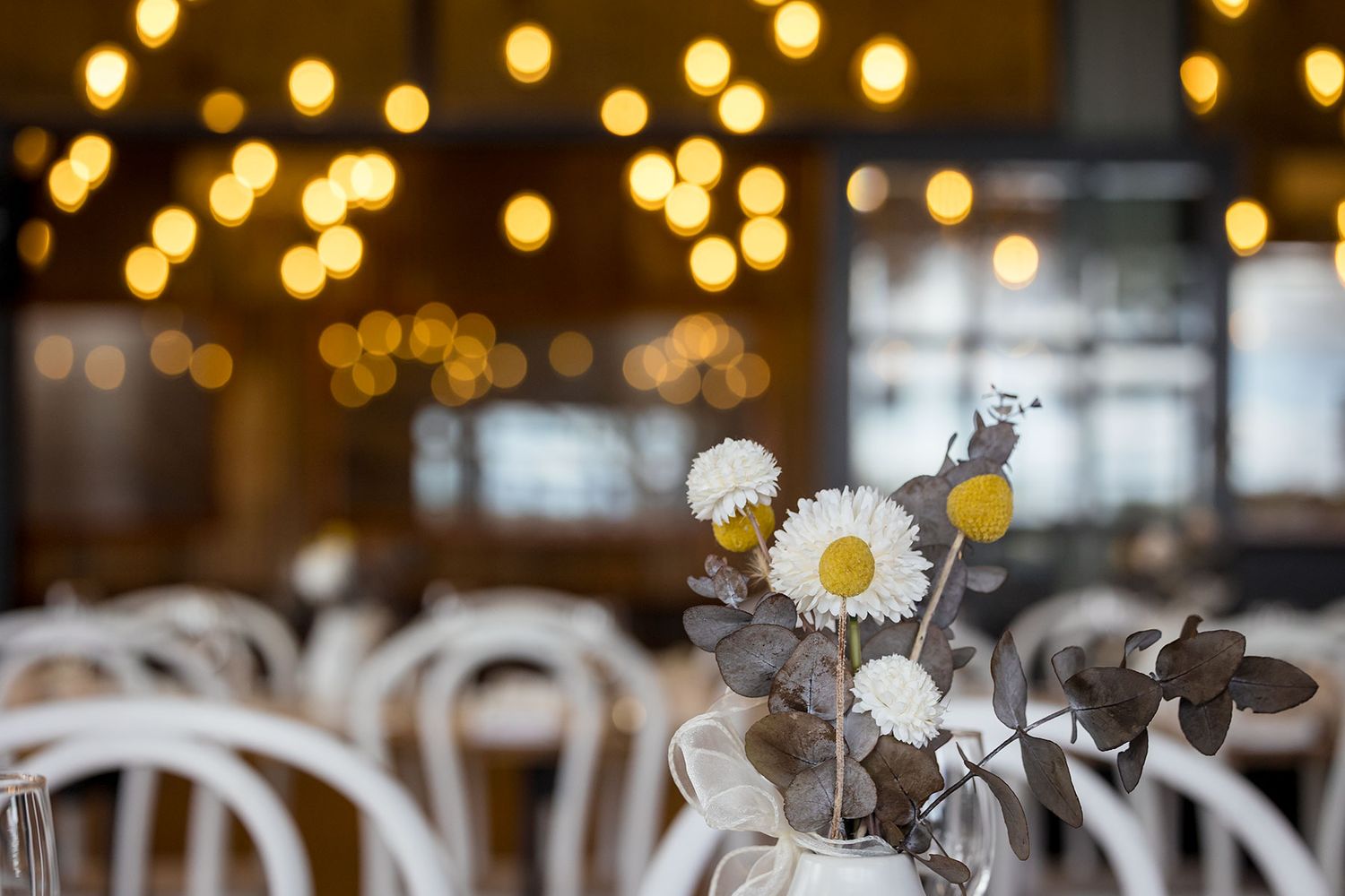 Elegant table setting with white bentwood chairs and floral centrepieces in white vases along a rustic linen tablecloth at Buller Wines.
