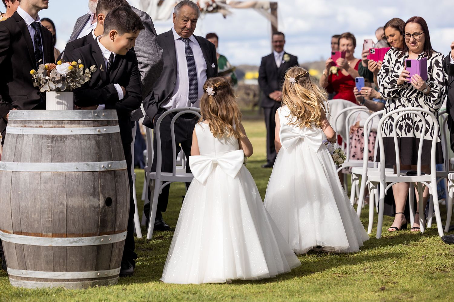 Guests mingle at an outdoor wedding reception featuring rustic wine barrels on grassy grounds amid elegant decor at Buller Wines