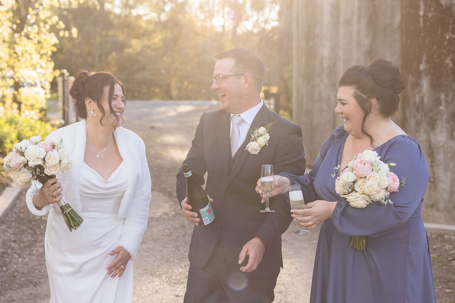 Groom holding a bottle of Champagne with his Bride and the maid of honour at Buller Wines.