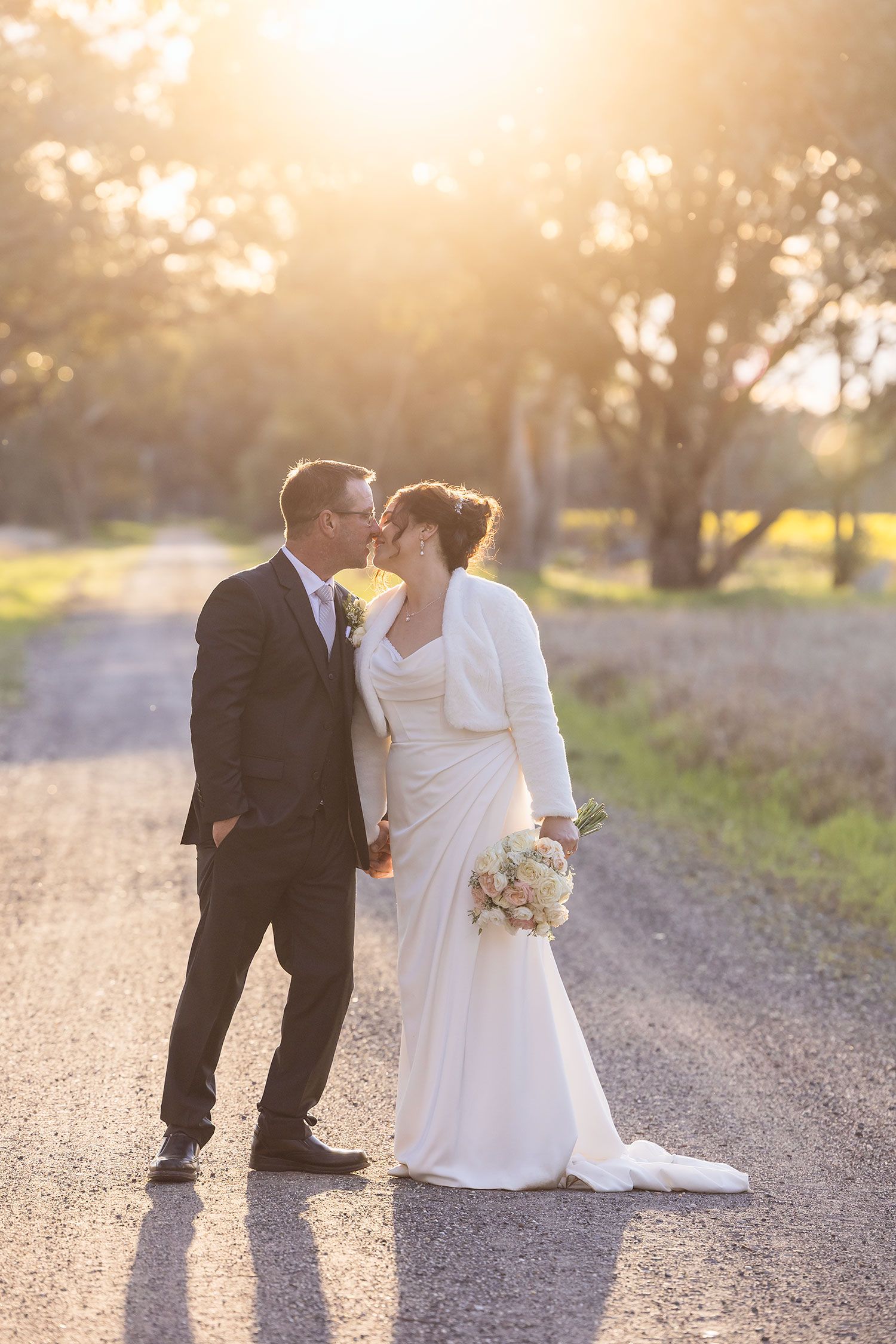 A romantic outdoor wedding photo of a Bride and Groom taken at sunset on a dirt road with warm golden lighting at Buller Wines.