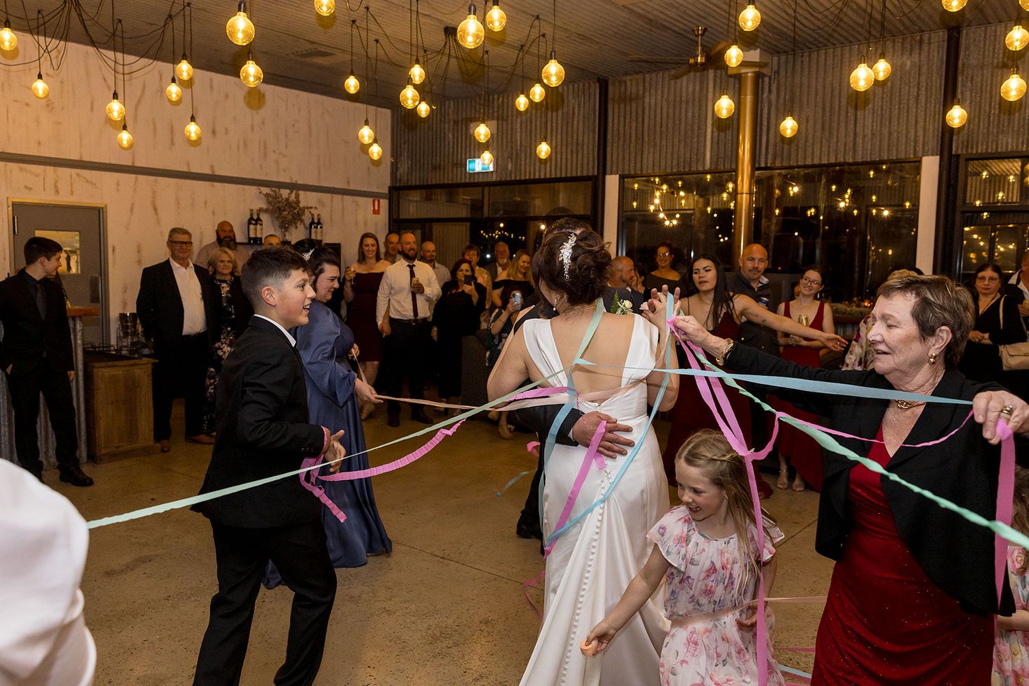 Wedding guests dance and wrap the wedding couple in coloured ribbons during their first dance at the wedding reception at Buller Wines.