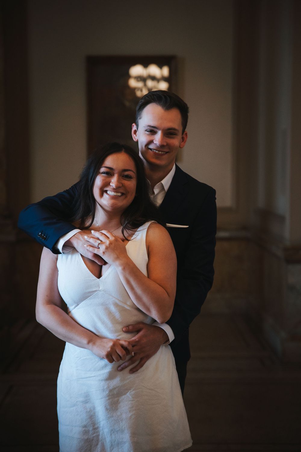A tender embrace captured in a dimly lit hallway with classic architectural elements.