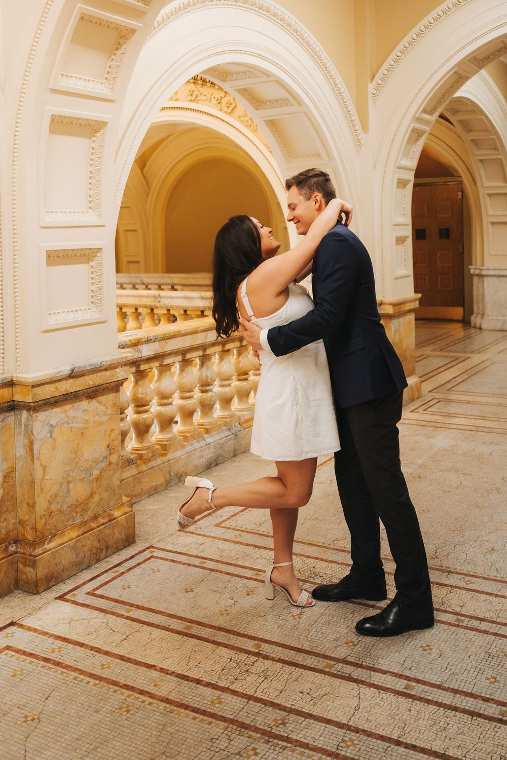 A romantic embrace in an ornate hallway with arched ceilings and marble details.