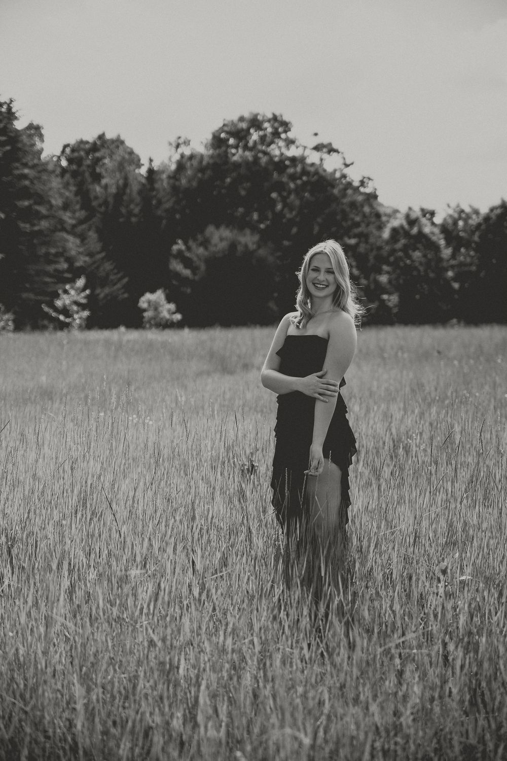 A black and white portrait in a serene meadow with tall grass and trees in the background.