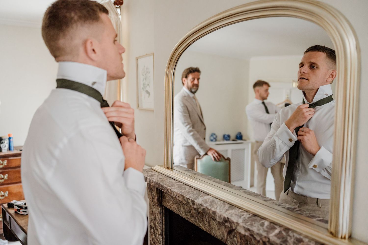 Groom getting ready with groomsmen in front of mirror before wedding ceremony.