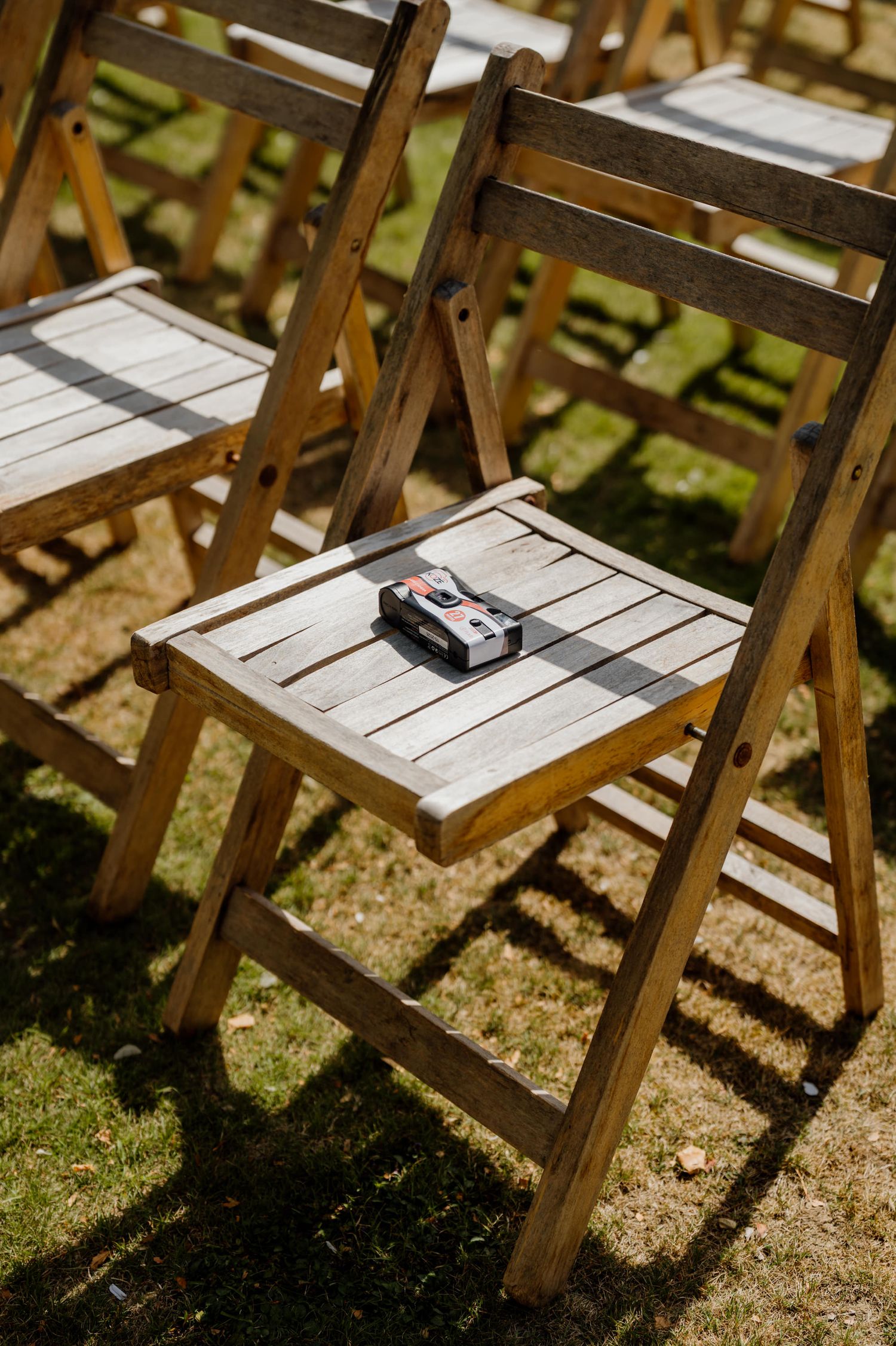 Wooden folding chairs set up in rows on grass casting strong shadows in sunlight.