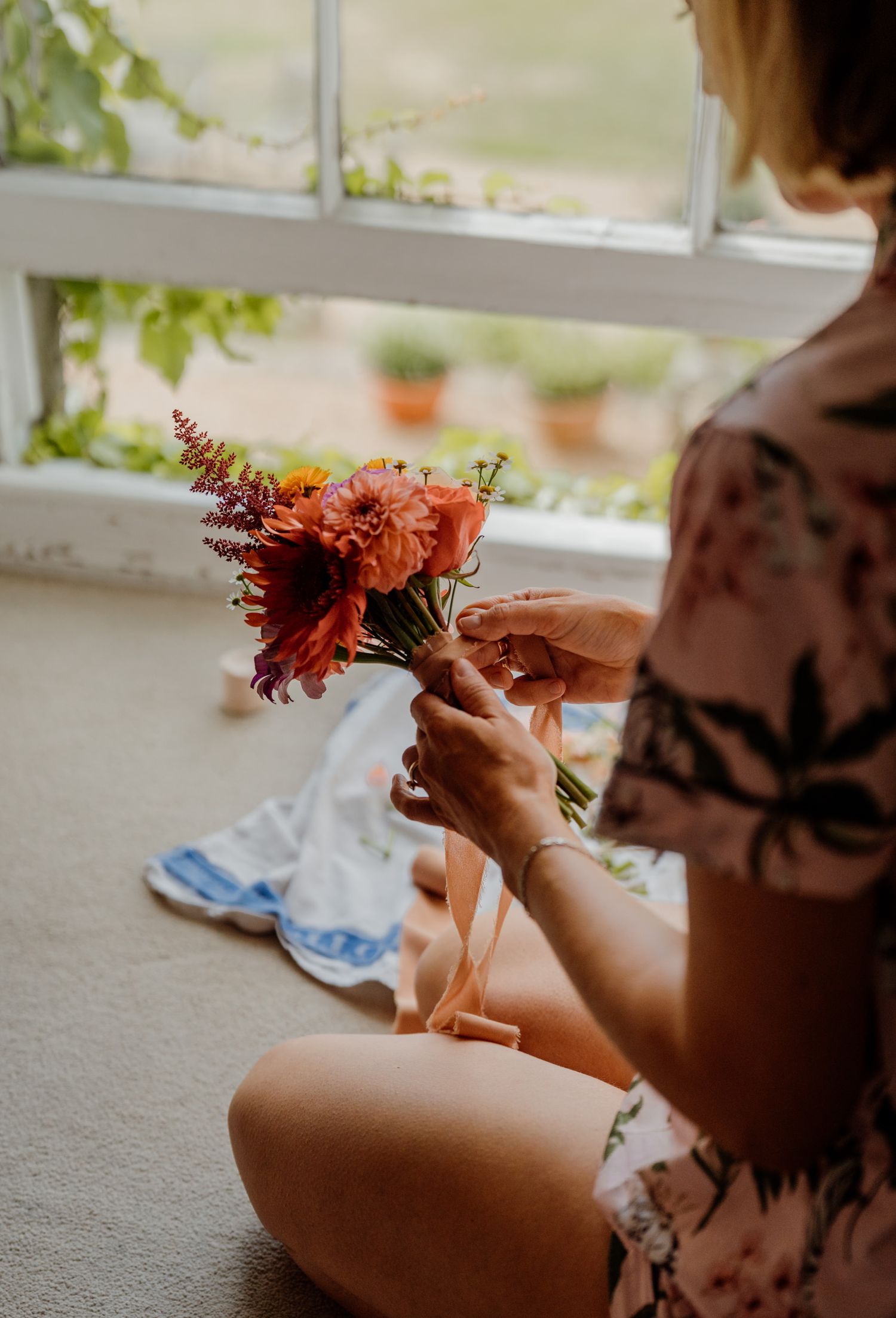 Close-up detail of hands arranging red and orange autumn flowers for a wedding bouquet.