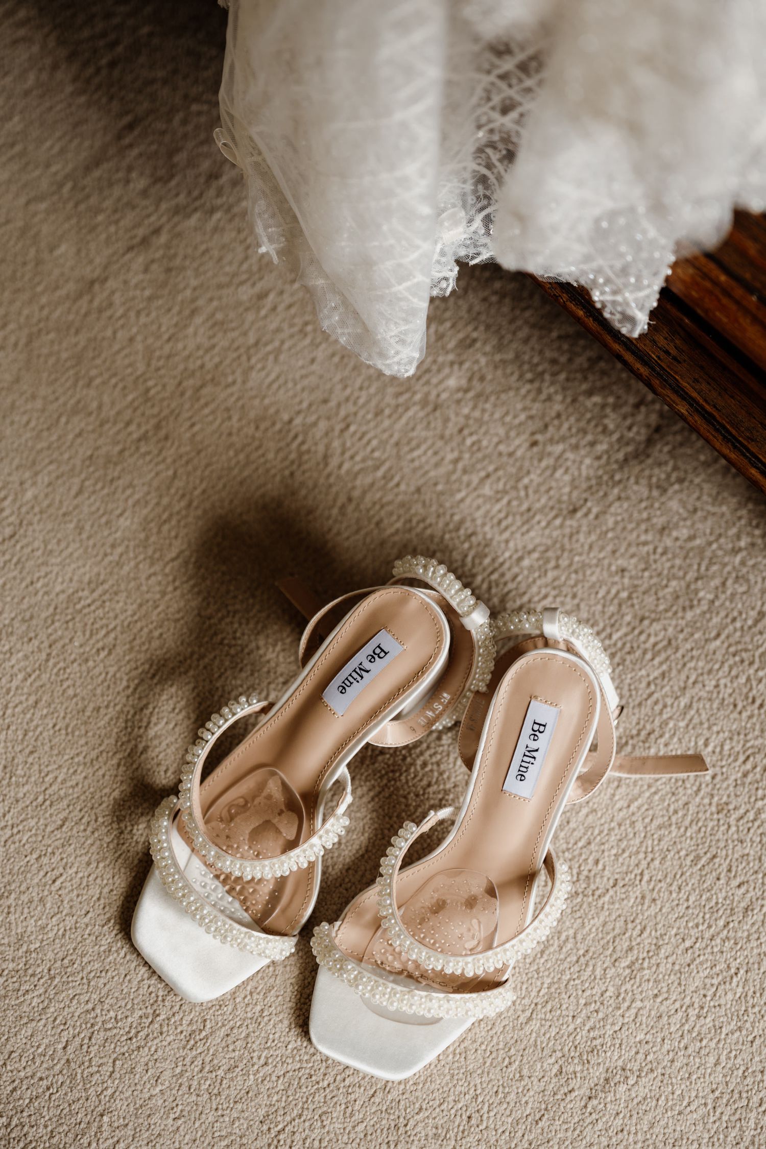 White bridal shoes with pearl details displayed on beige carpet.