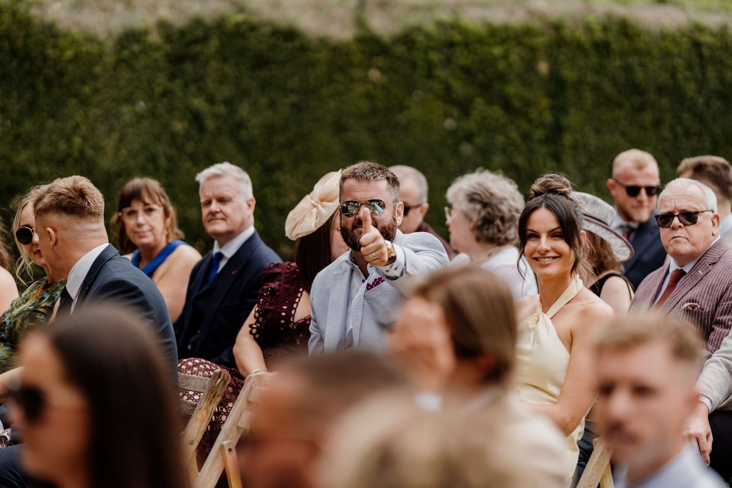 A crowd of wedding guests gathered outdoors watching a ceremony with focused attention.