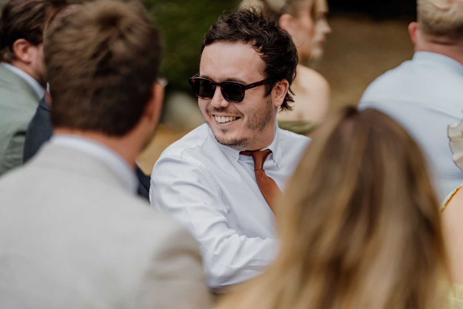 Wedding guest in sunglasses enjoying conversation at outdoor reception.