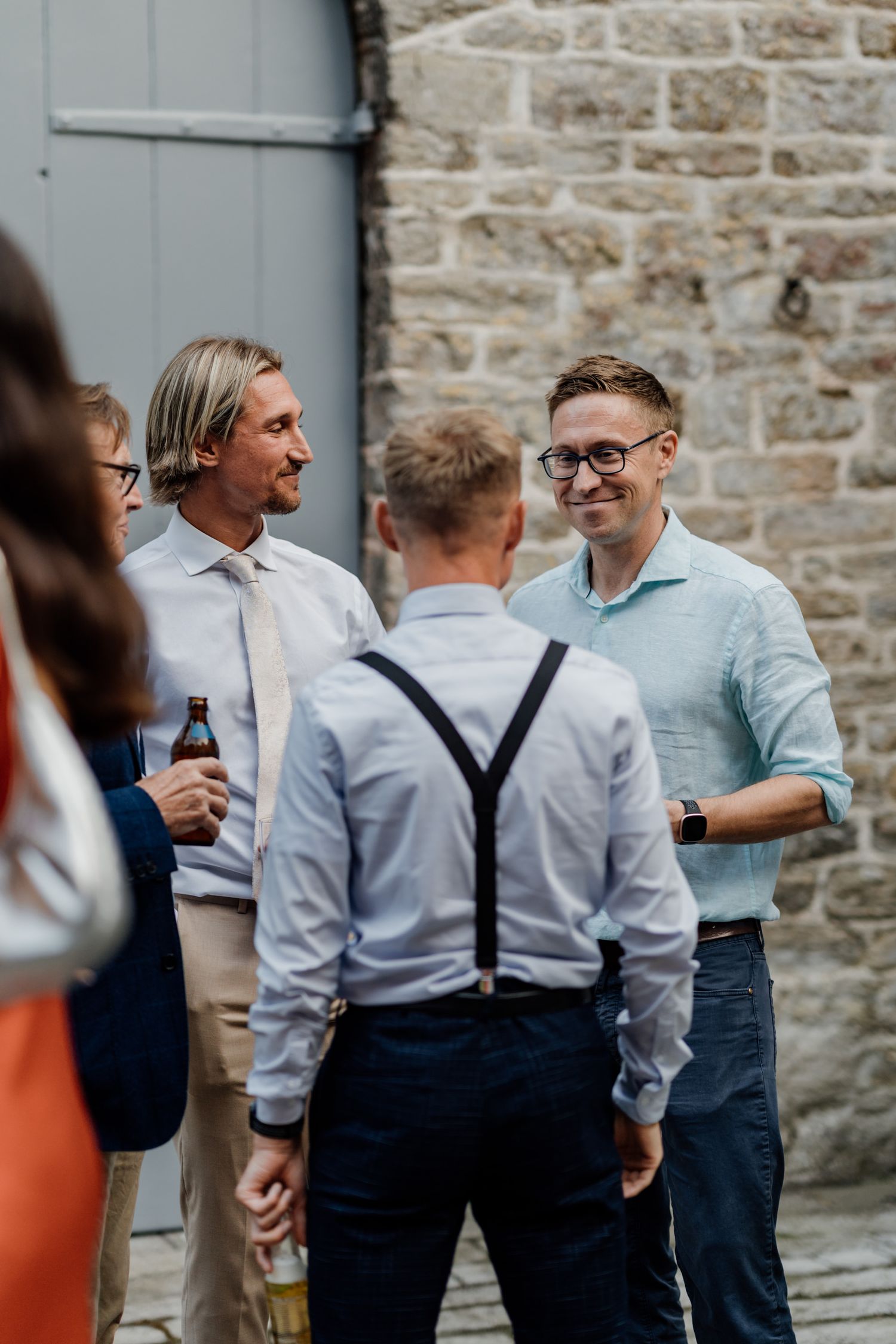 Groomsmen in suspenders and light blue shirts chatting before the ceremony.