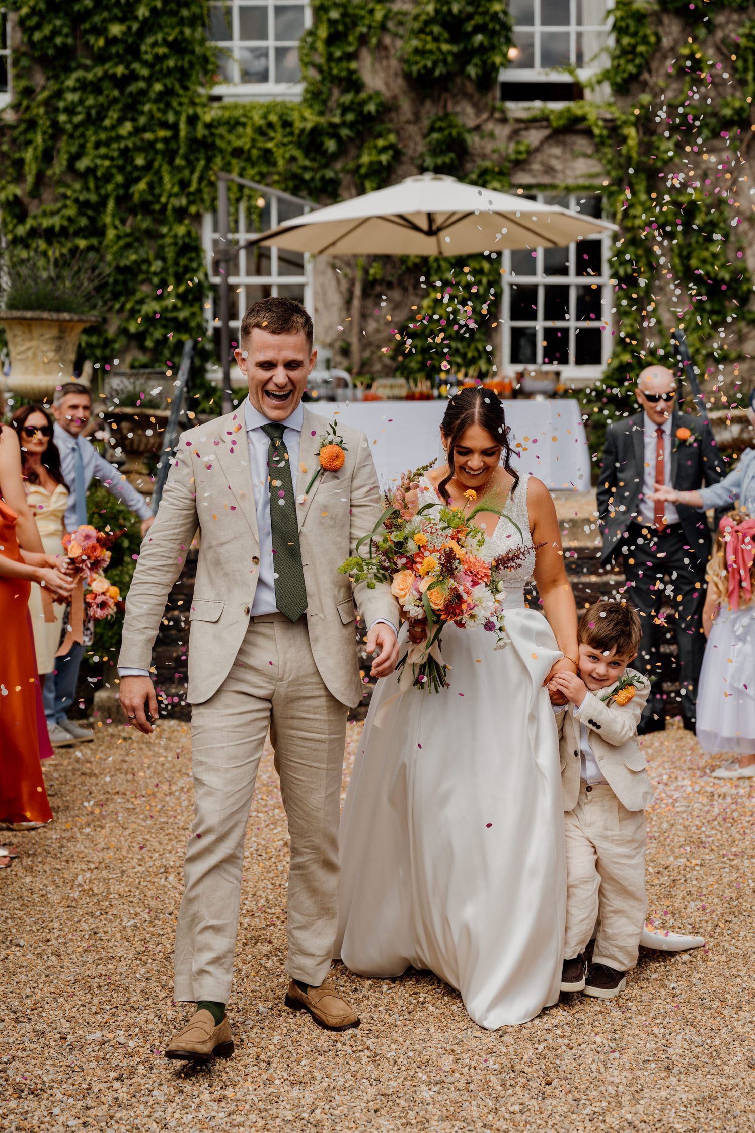 Wedding party celebrates with confetti in front of a historic building with ivy-covered walls.