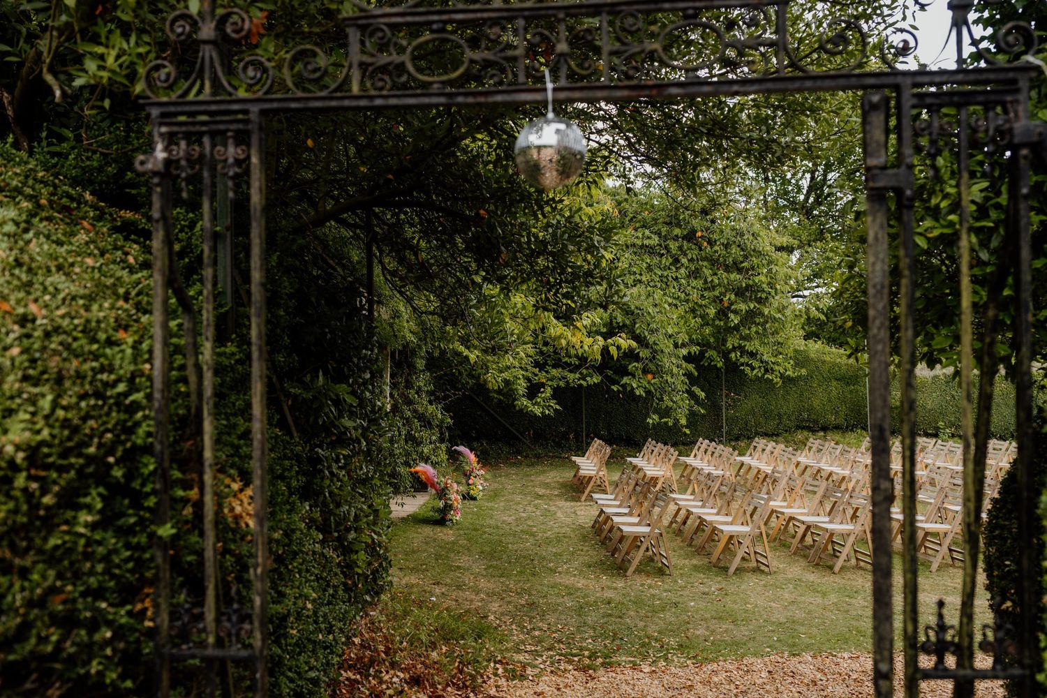 Wooden ceremony chairs line a rustic outdoor wedding venue path surrounded by lush greenery and trees.