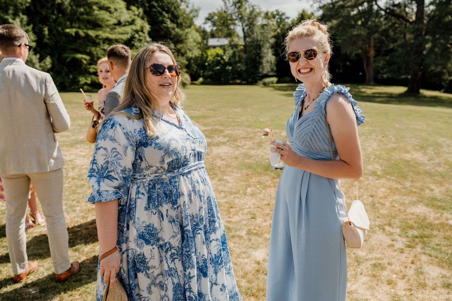 Guests in blue and grey attire celebrate at an outdoor summer wedding reception on a sunny day.