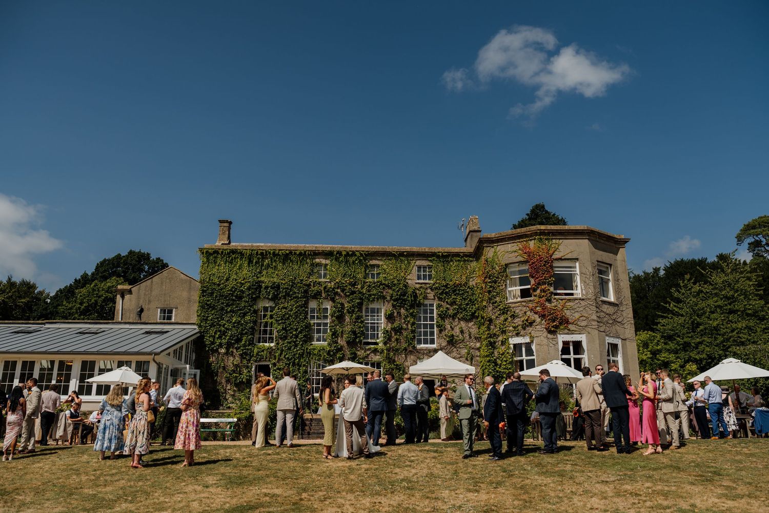 Wide panoramic view of a stone mansion wedding venue with guests gathered outside.