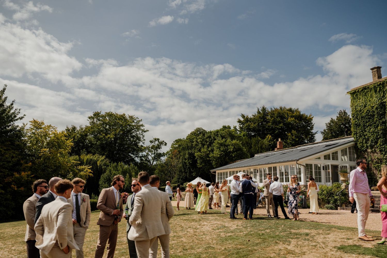 Wedding guests gather outside on a sunny day for an outdoor summer celebration at a rural venue.