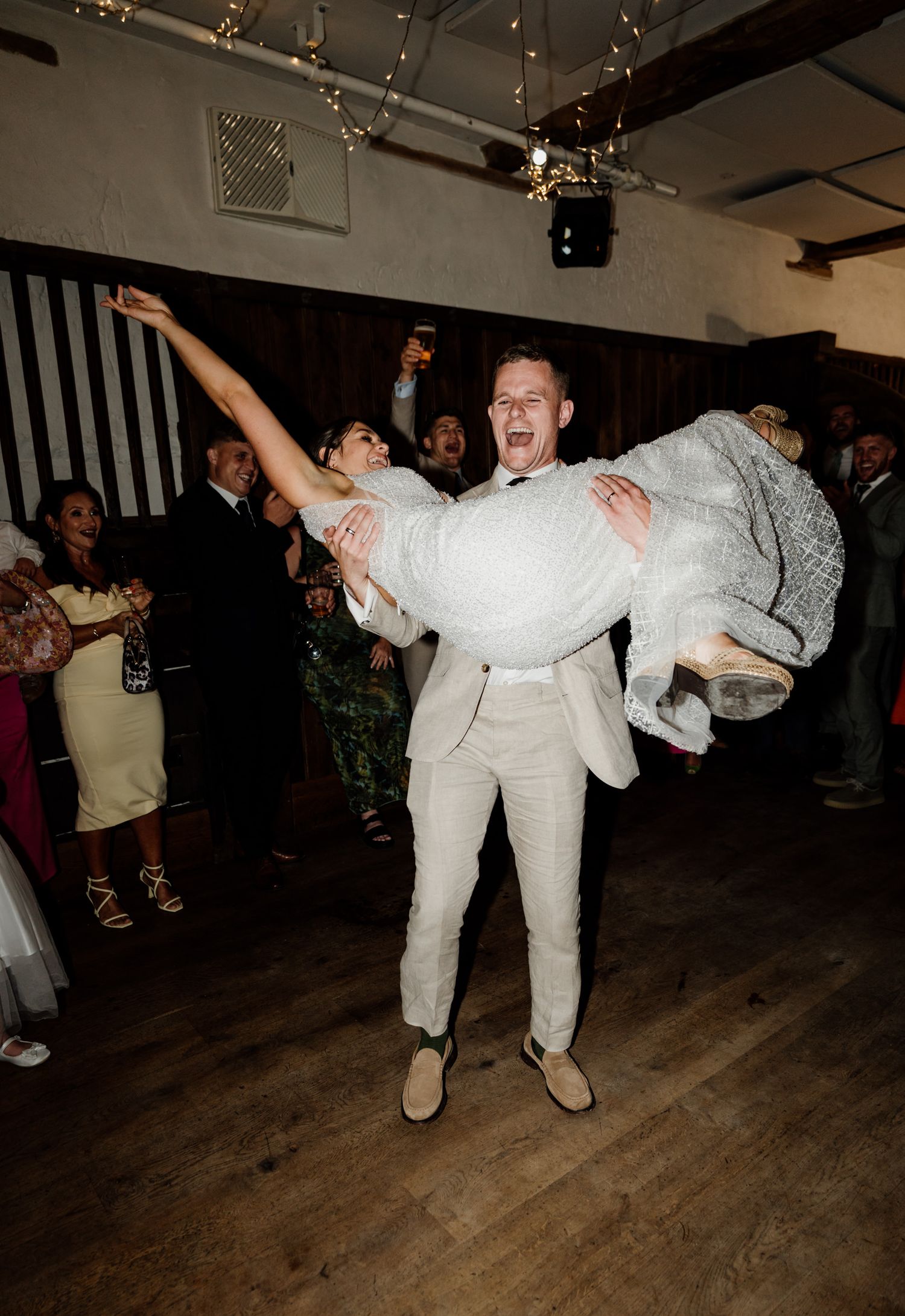 Dancing couples at a wedding reception in a dimly lit indoor venue with string lights overhead.