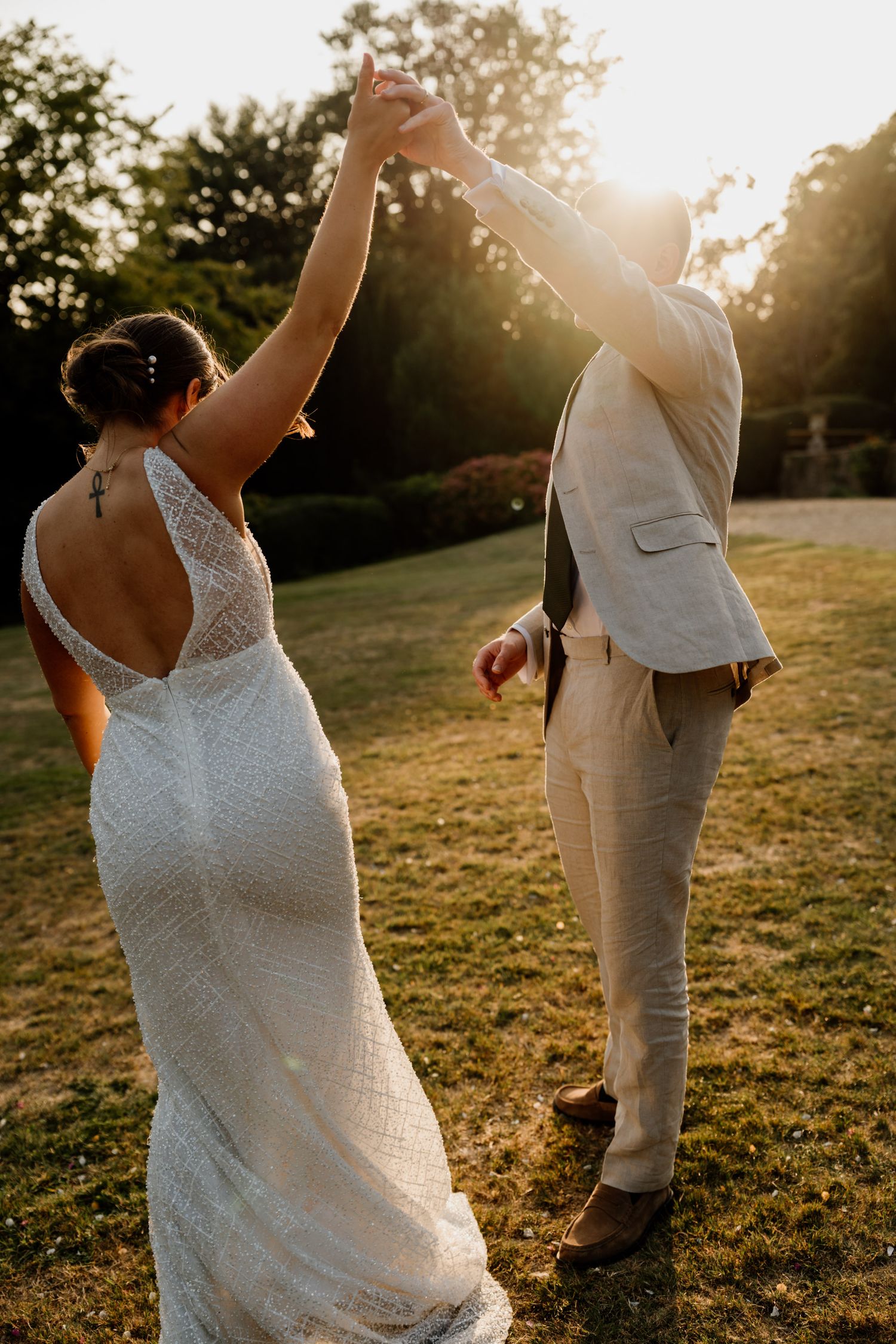 A wedding couple dances and spins in a sunlit field during golden hour.