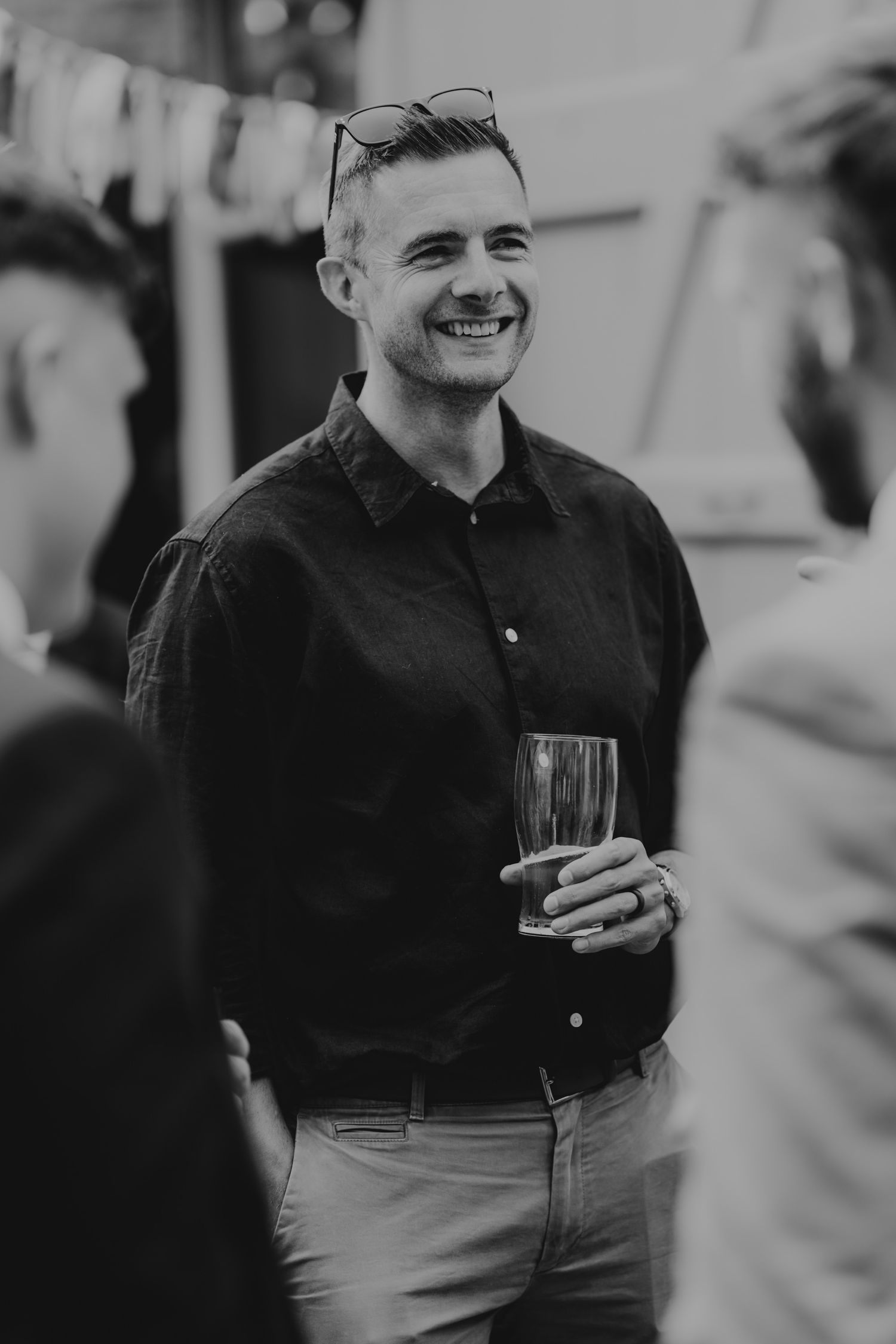 A black and white candid photo captures guests laughing and enjoying drinks at a social gathering.