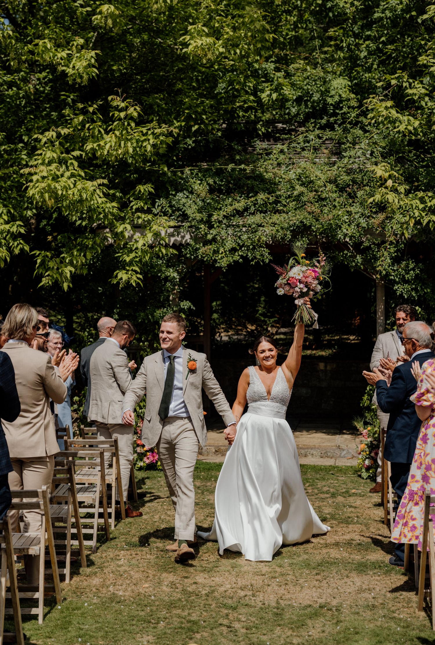 Panoramic view of an outdoor wedding ceremony with wooden chairs and greenery backdrop.
