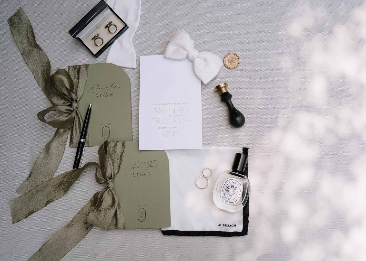 Styled wedding flat lay with sage stationery, bow tie, perfume, ring, and ribbon details.