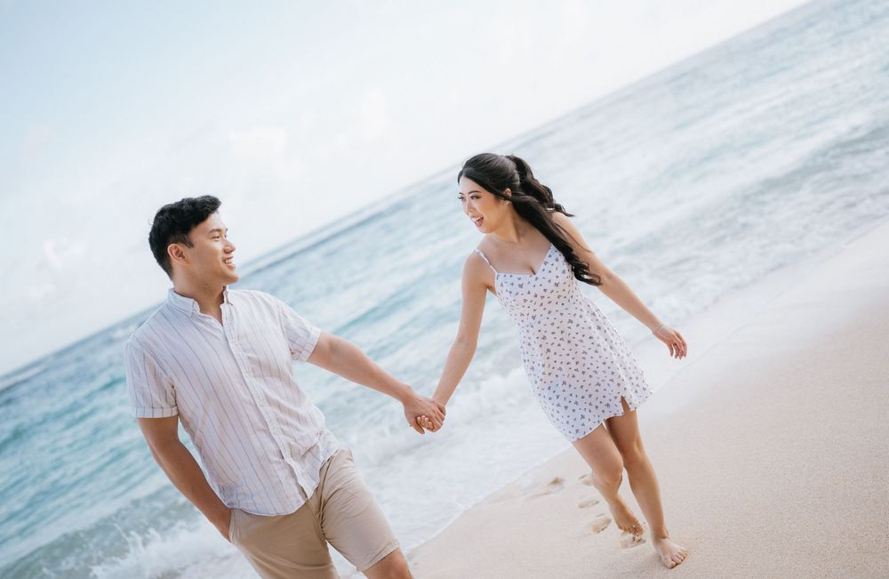 Couple walking hand in hand along a serene beach with waves and sand in soft lighting.