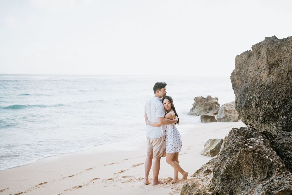 Couple enjoying a tender moment near rocky cliffs on a peaceful beach.