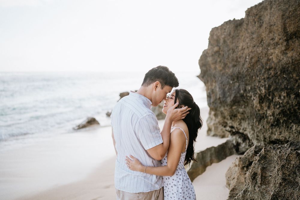 Intimate beach portraits with couple embracing near coastal rock formations.