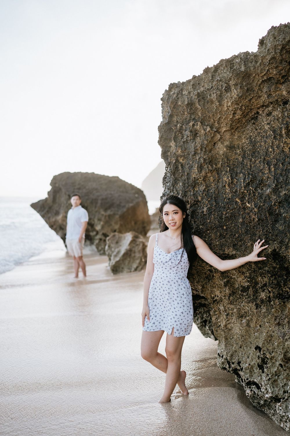 Playful beach photoshoot with person in polka dot outfit posing by coastal rocks.