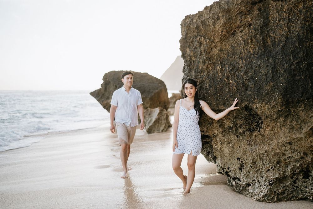 Romantic beach photography with couple walking near dramatic coastal cliffs.
