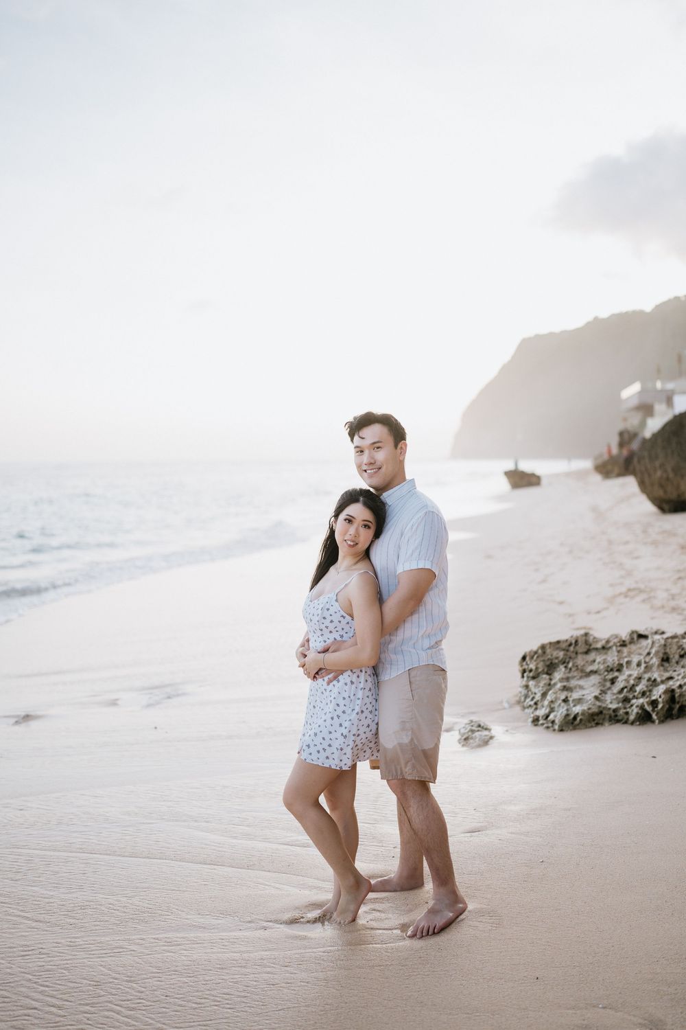 Intimate beach portraits with couple embracing on sandy shoreline at sunset.