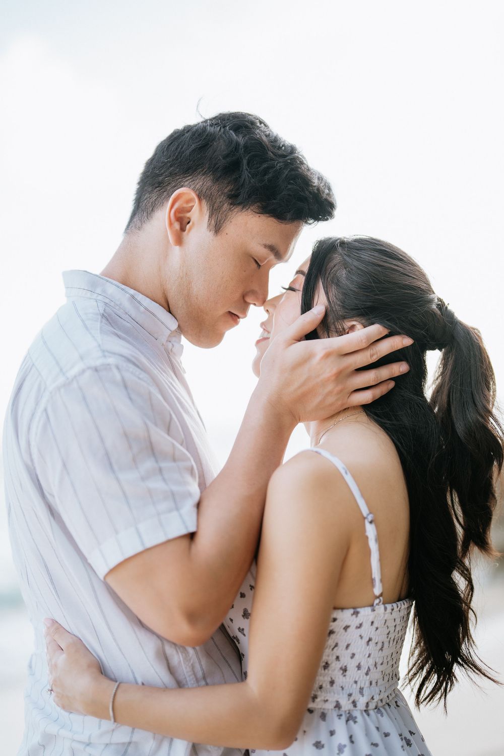 Intimate couple sharing tender moments against a bright coastal backdrop.