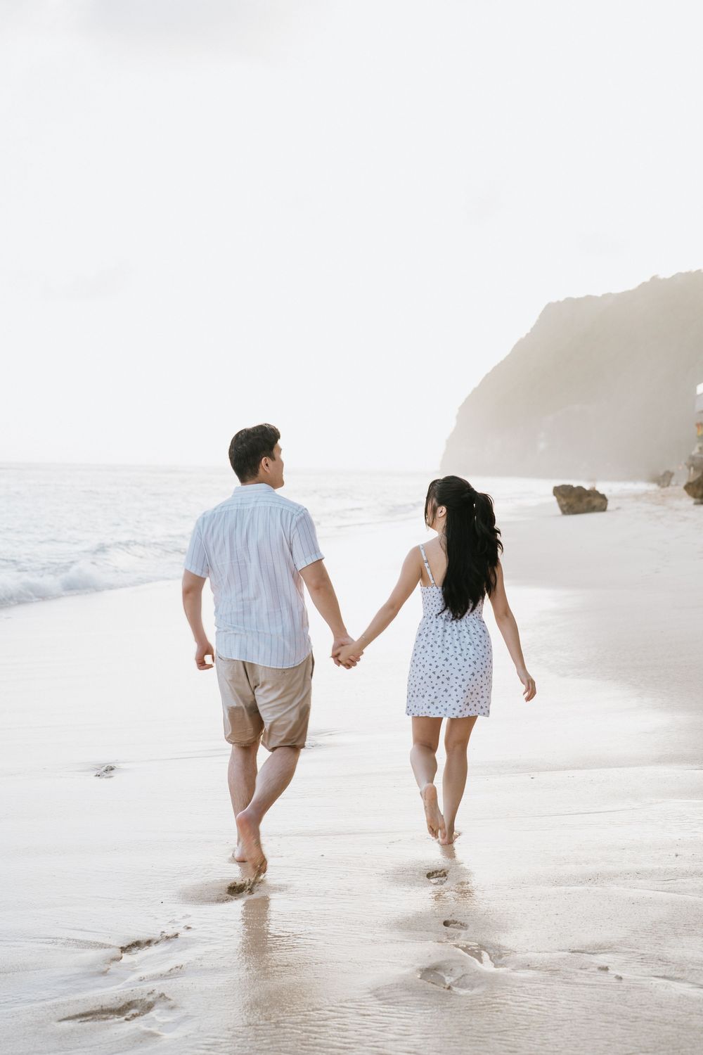 Couple taking a romantic stroll along the shoreline leaving footprints in the wet sand.