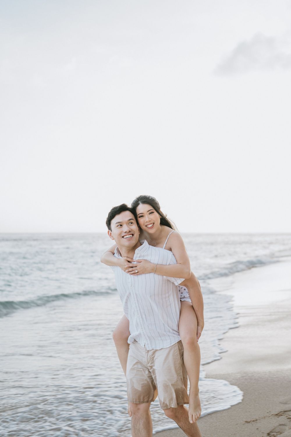 Playful couple enjoying a piggyback ride along the sandy shoreline.