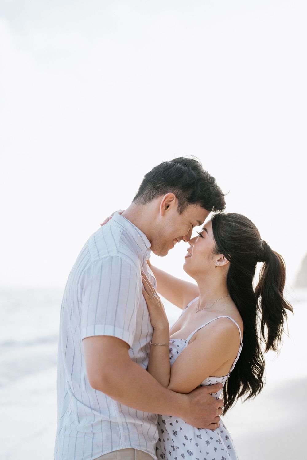 Couple sharing an intimate embrace on a bright, misty beach.