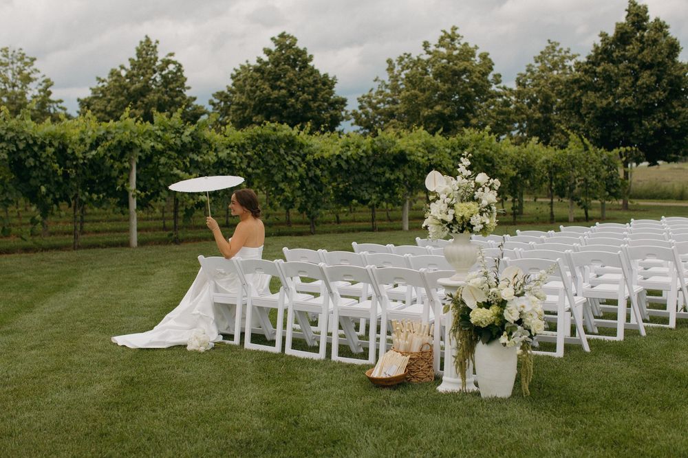 White wedding ceremony chairs set up on a lawn with vineyard and trees in the background.