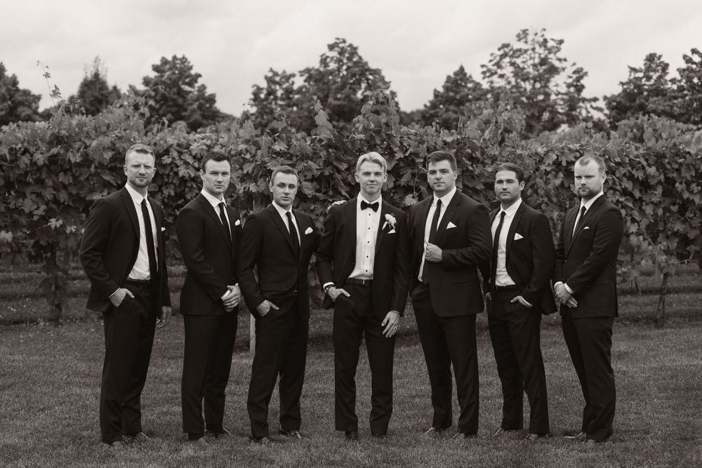 A wedding party in black tuxedos poses together outdoors.