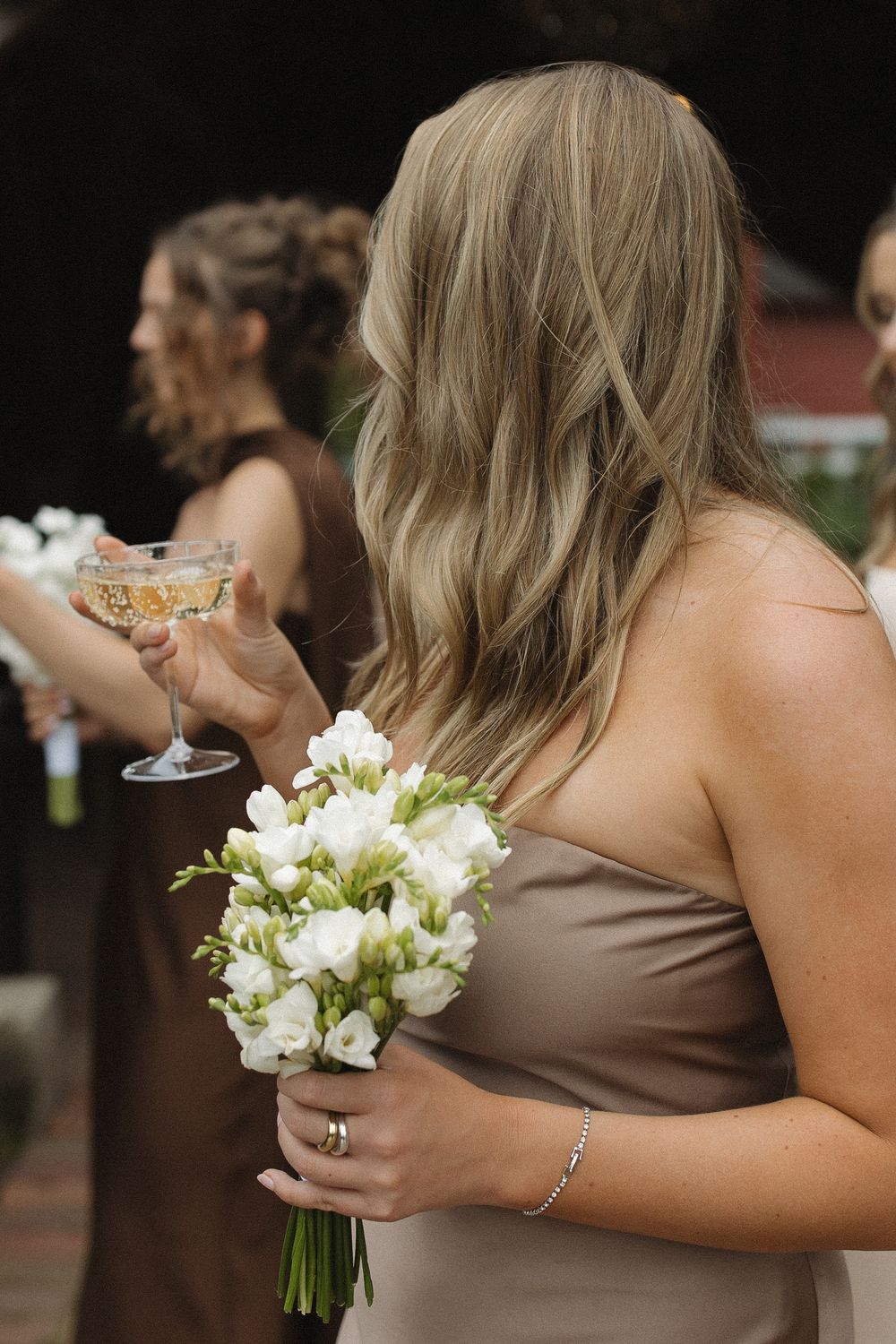 Bridesmaids in brown dresses hold white floral bouquets during wedding celebration.