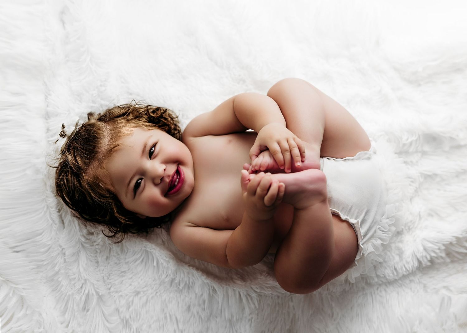 Baby wearing green overalls lays on white paper in a progression of closeup studio portraits from different angles.