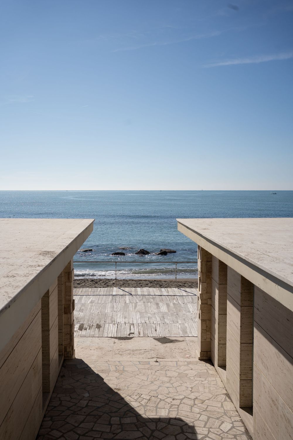 Modern concrete pathway overlooking a scenic ocean view with rocks and clear blue sky on the horizon.
